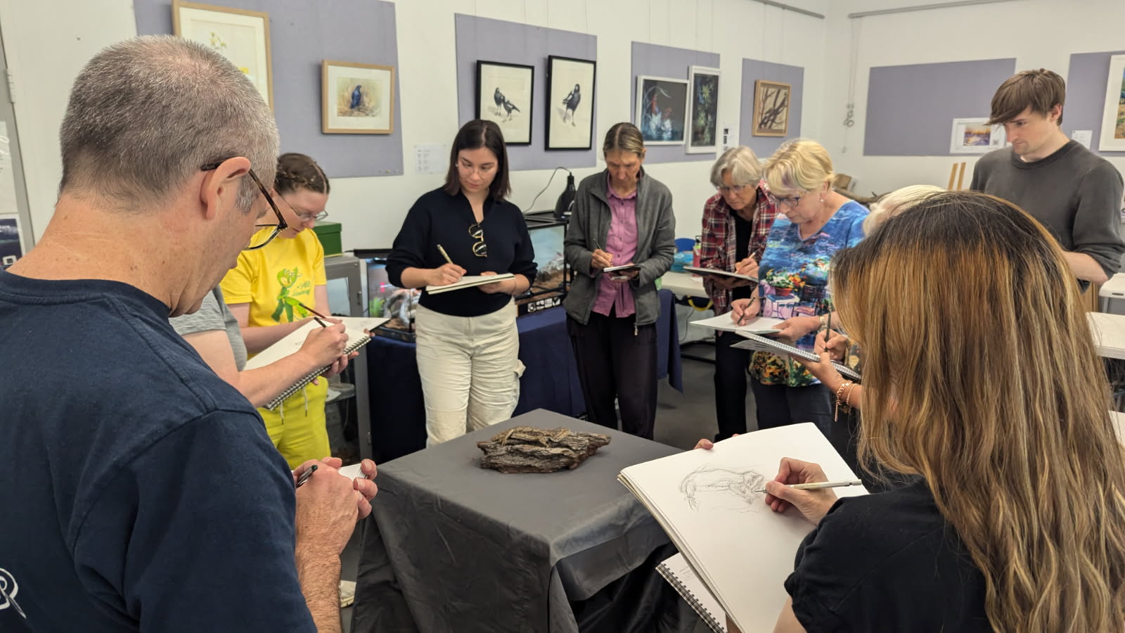 students of the NatureArt Lab Workshop Illustrating Reptiles with Zoe Lawrence stand around a table drawing a Bearded Dragon
